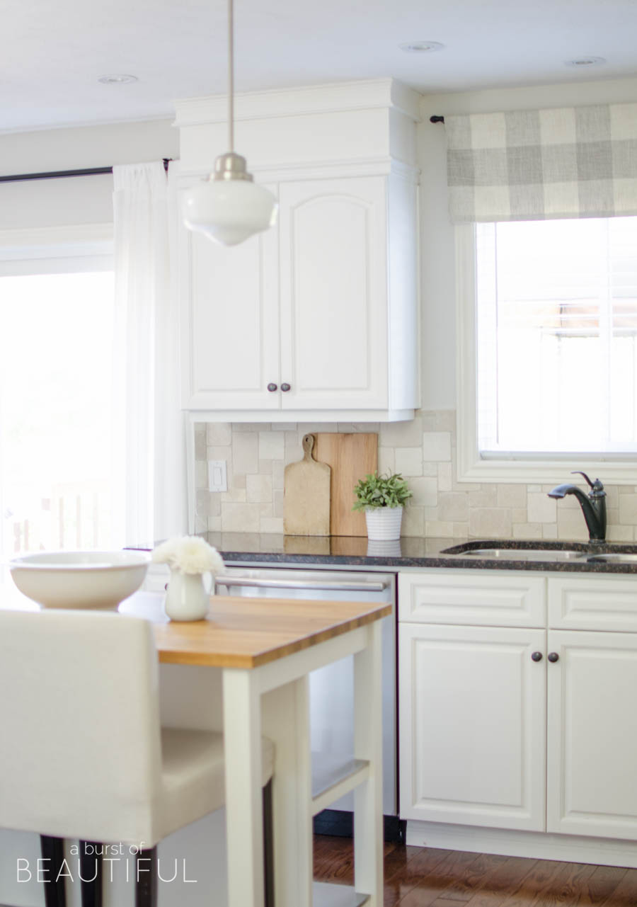 This simple farmhouse kitchen is the heart of this busy family's home. White cabinets, black granite counters and natural wood elements add plenty of texture and charm to this bright and airy space. 