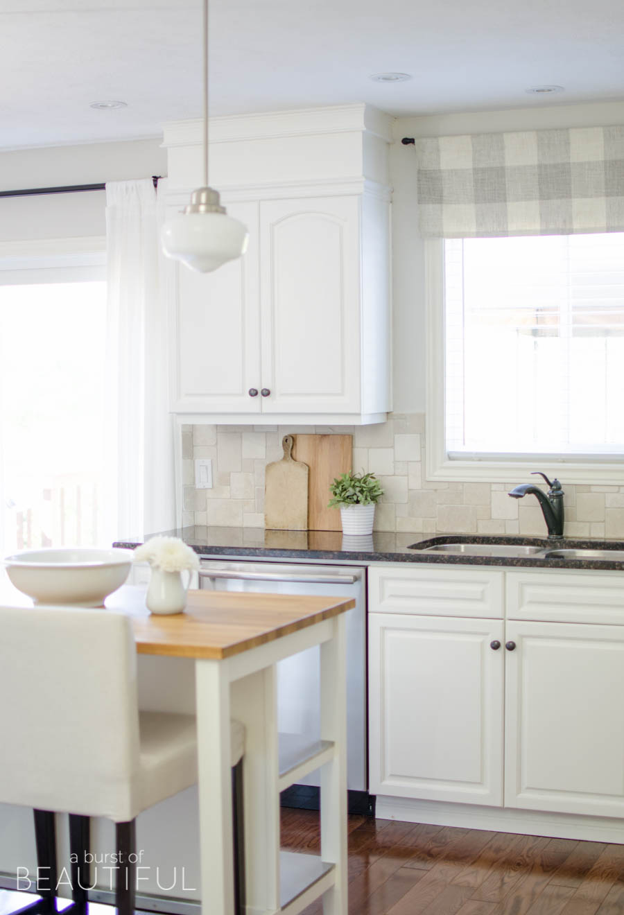 This simple farmhouse kitchen is the heart of this busy family's home. White cabinets, black granite counters and natural wood elements add plenty of texture and charm to this bright and airy space. 