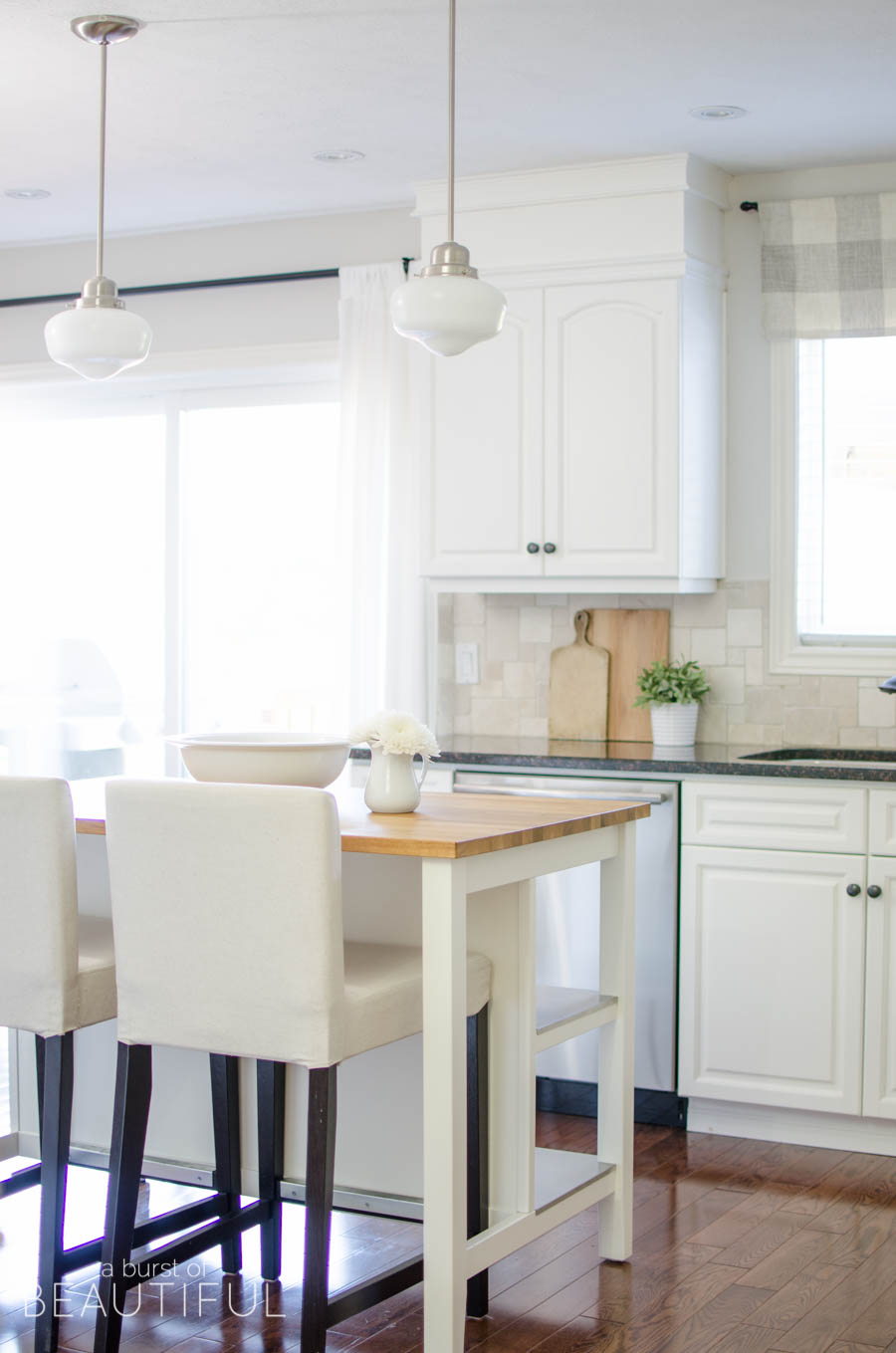 This simple farmhouse kitchen is the heart of this busy family's home. White cabinets, black granite counters and natural wood elements add plenty of texture and charm to this bright and airy space. 