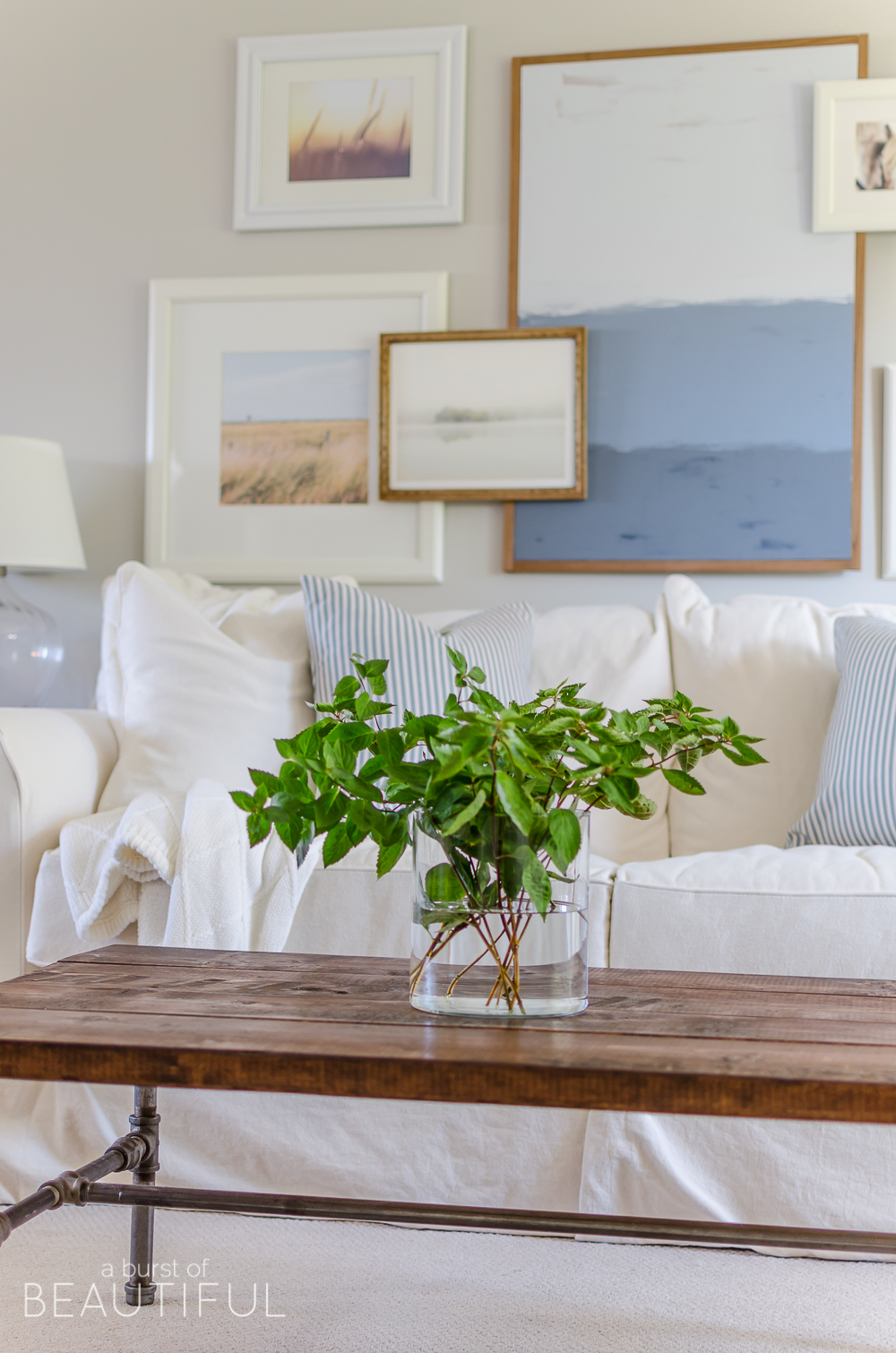 A white slipcovered sofa, layered gallery wall and natural wood elements help this charming farmhouse living room feel cozy and inviting. 