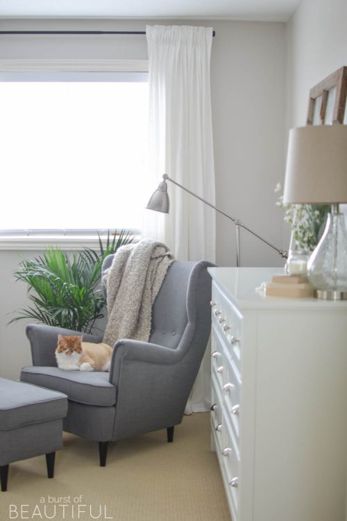 A neutral farmhouse bedroom welcomes spring with classic white bedding, a grey wingback chair and subtle pops of color | A Burst of Beautiful
