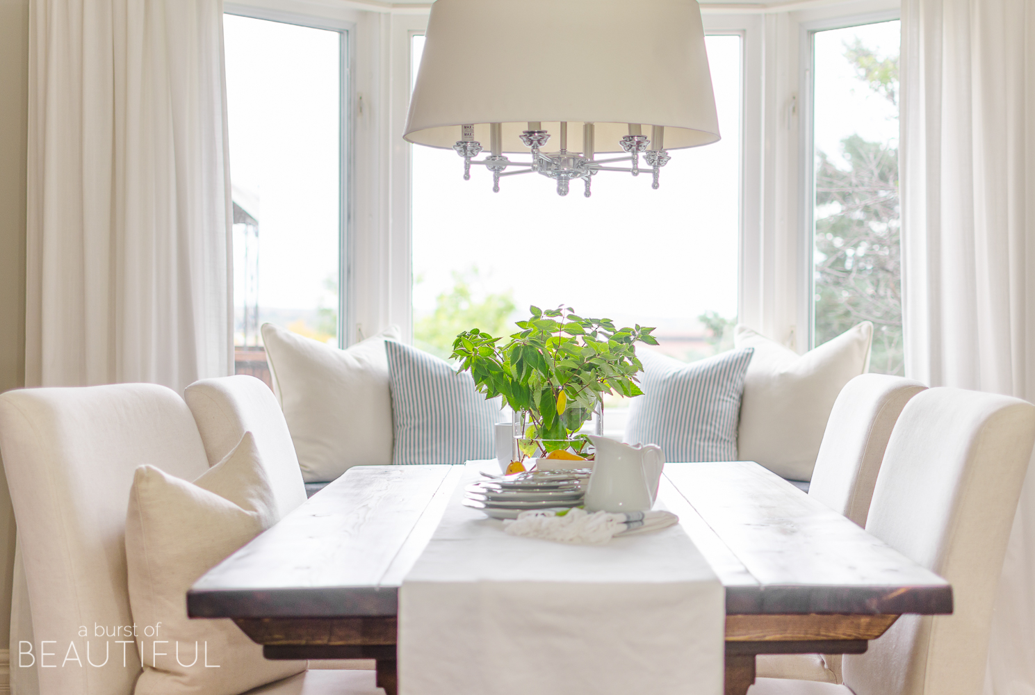 A bright and inviting dining room boasts simple farmhouse style with a DIY farmhouse dining table and classic window bench. 