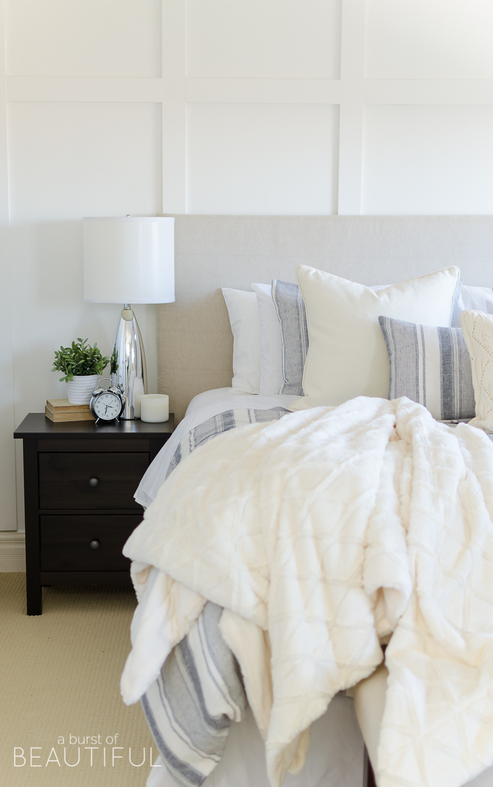 This cozy farmhouse master bedroom features a beautiful DIY shiplap fireplace, indigo ticking strip bedding and woven wood shades.