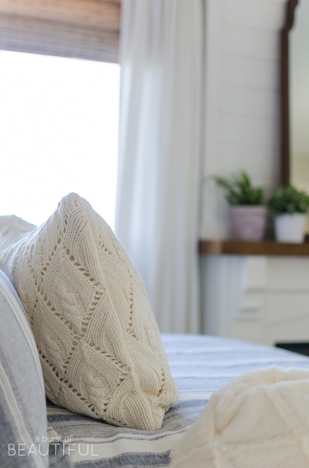 This cozy farmhouse master bedroom features a beautiful DIY shiplap fireplace, indigo ticking strip bedding and woven wood shades.