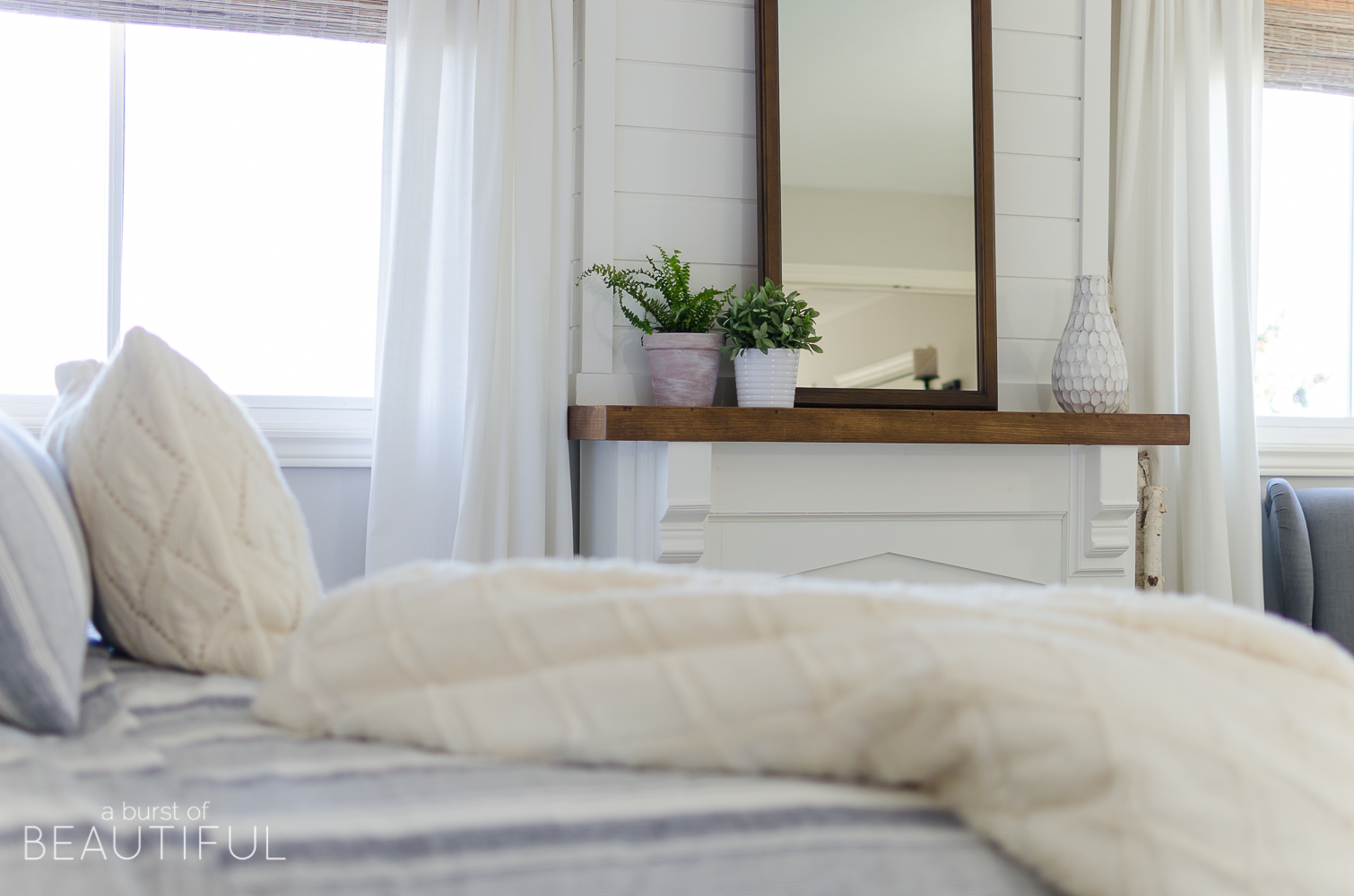 This cozy farmhouse master bedroom features a beautiful DIY shiplap fireplace, indigo ticking strip bedding and woven wood shades. 