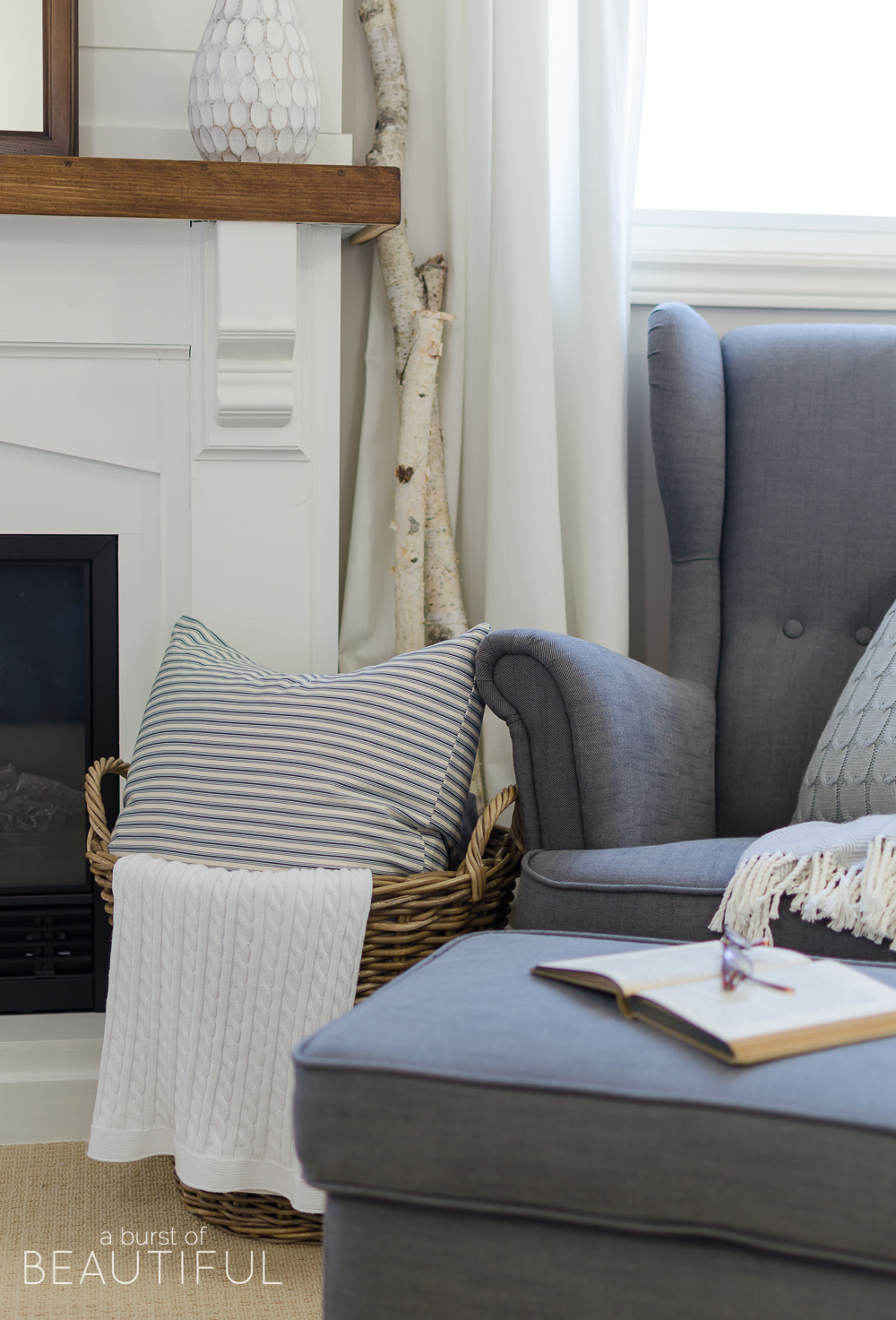 This cozy farmhouse master bedroom features a beautiful DIY shiplap fireplace, indigo ticking strip bedding and woven wood shades.