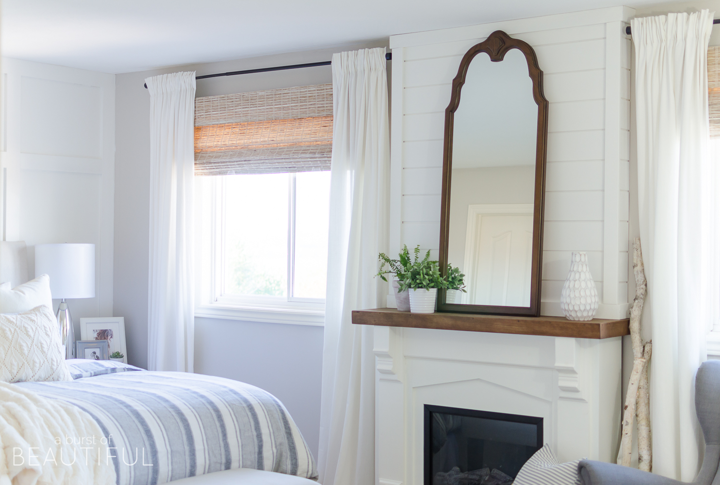 This cozy farmhouse master bedroom features a beautiful DIY shiplap fireplace, indigo ticking strip bedding and woven wood shades. 