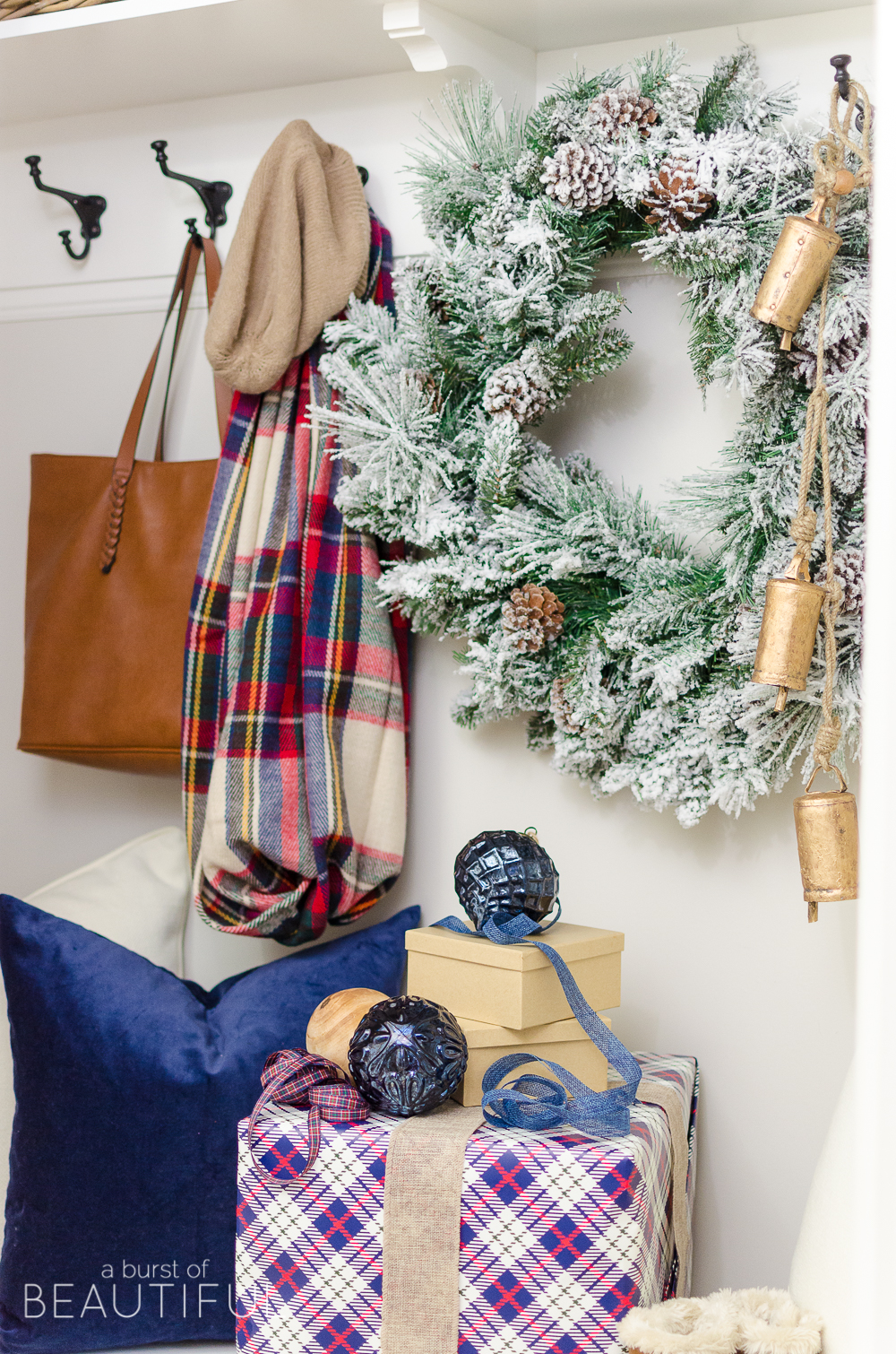 A simple Christmas entryway receives a dose of holiday charm with a flocked wreath, velvet pillows and packages wrapped in festive Christmas paper. 