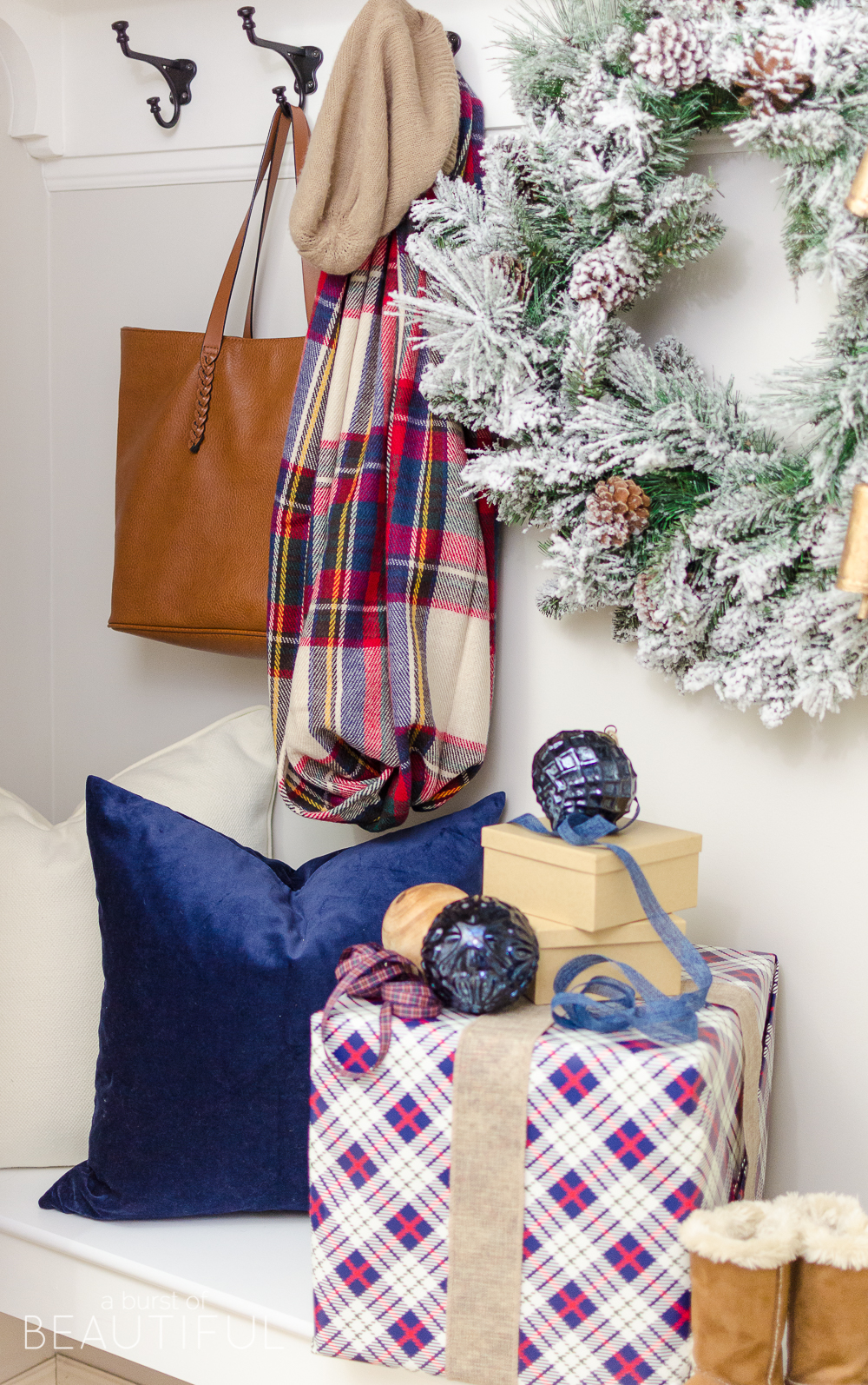 A simple Christmas entryway receives a dose of holiday charm with a flocked wreath, velvet pillows and packages wrapped in festive Christmas paper. 