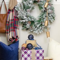 A simple Christmas entryway receives a dose of holiday charm with a flocked wreath, velvet pillows and packages wrapped in festive Christmas paper.