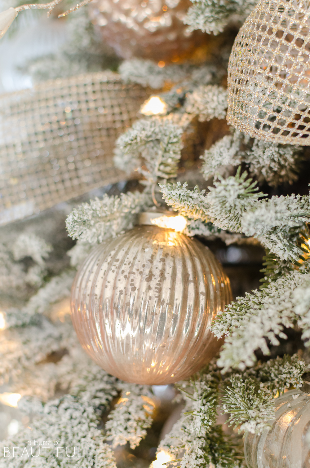 A snowy flocked Christmas tree decorated in silver and rose gold adds a big dose of holiday cheer to this modern farmhouse living room