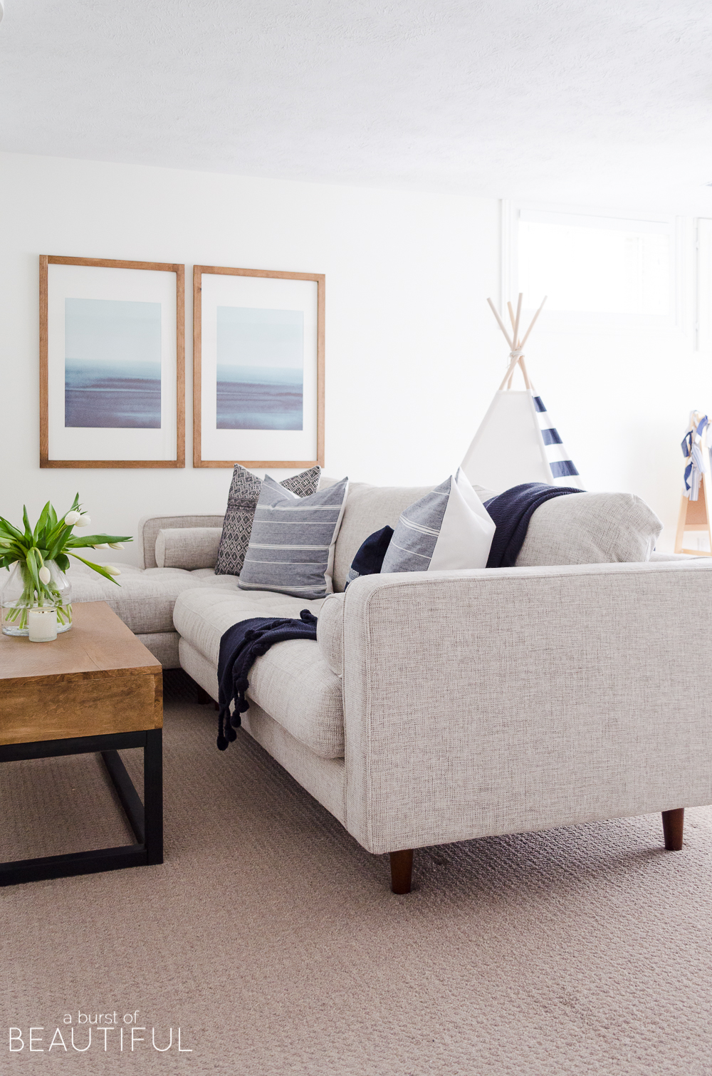 A bright family room features the perfect mix of traditional and modern design elements, including a mid-century modern sofa, open shelving and shiplap walls.