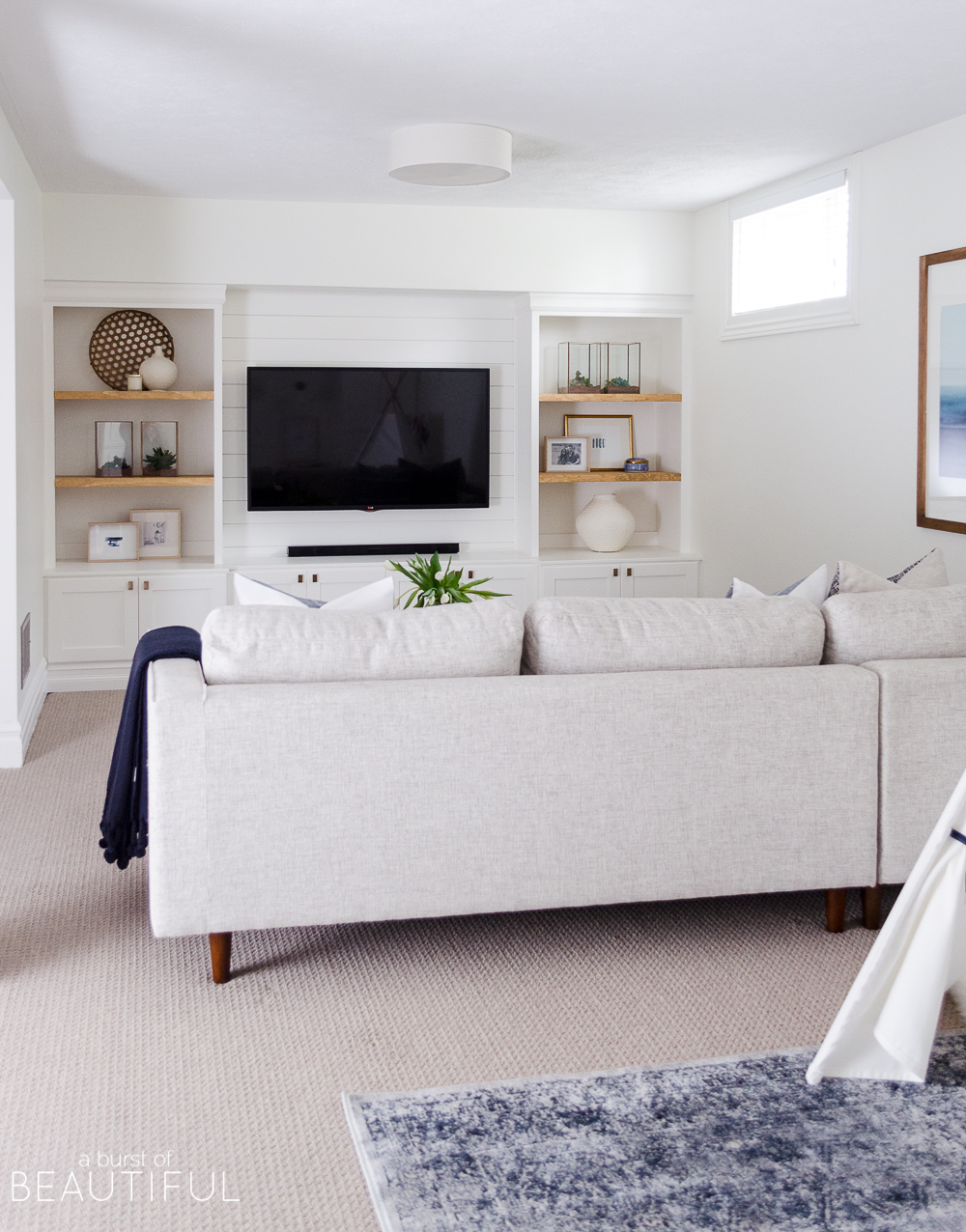 A bright family room features the perfect mix of traditional and modern design elements, including a mid-century modern sofa, open shelving and shiplap walls.