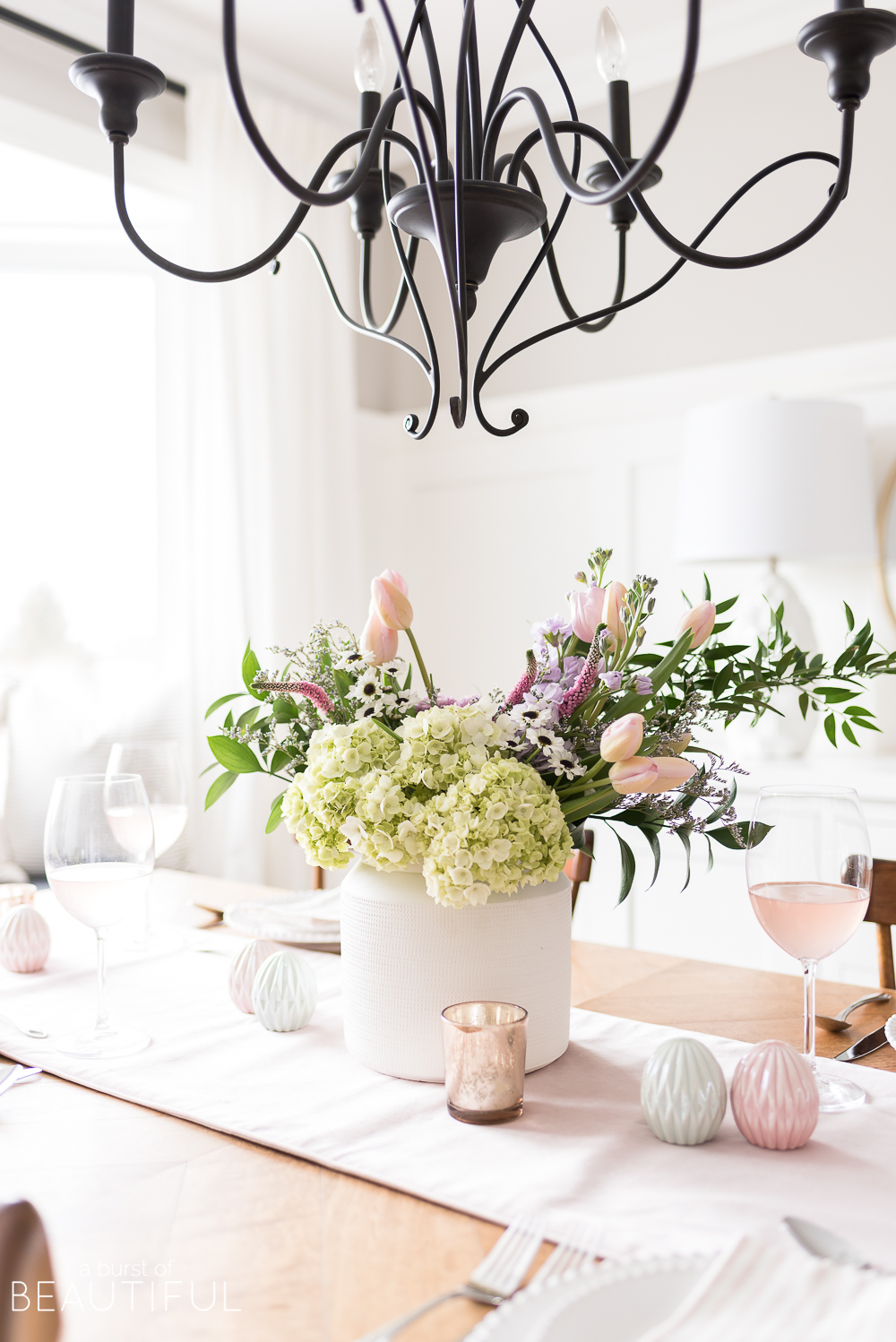 Celebrate Easter around a table set with classic white dishes, linens in pastel shades and a centerpiece full of spring blooms. 