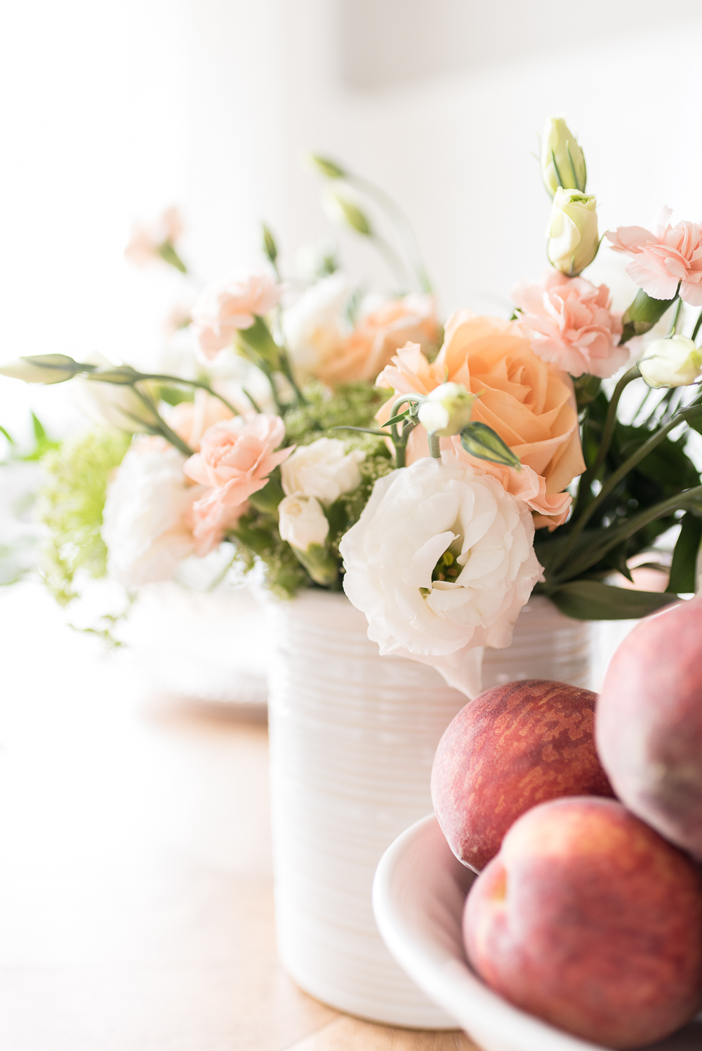 Fresh flowers in soft peach, blush and cream hues paired with a bowl of juicy peaches make an effortless centerpiece for a simple summer gathering.